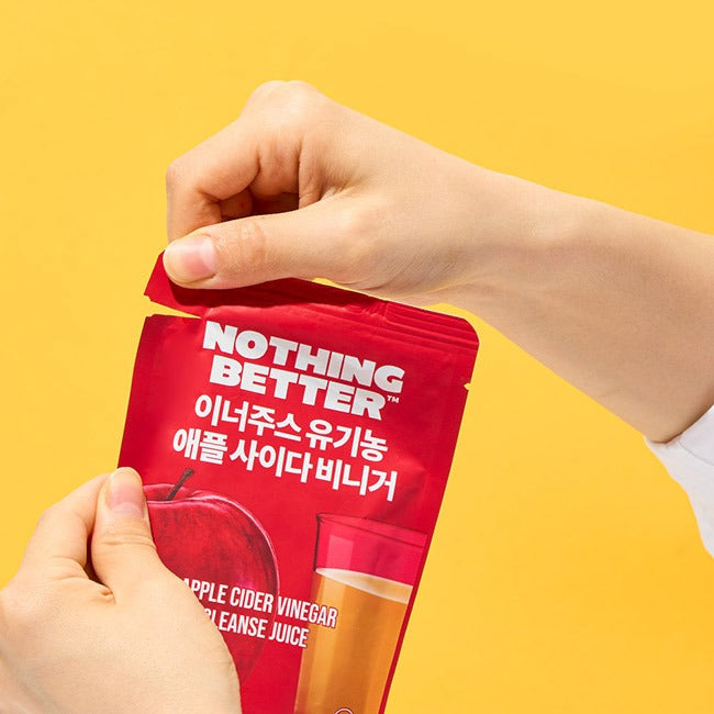 Hands opening NOTHING BETTER Inner Juice Apple Cider Vinegar Cleanse Juice (X24) pouch against yellow background.