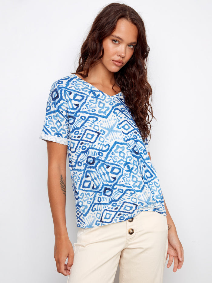 Blue patterned top with a V-neckline, paired with beige pants. Features short sleeves for a relaxed look by Charlie B.