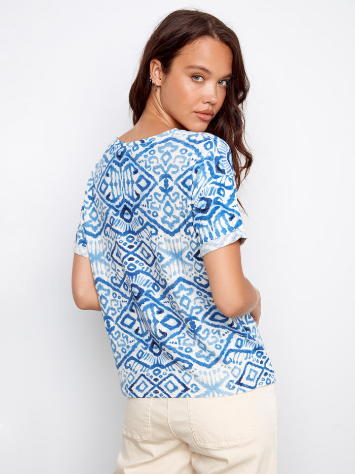 Elegant blue top highlighted by its unique pattern and V-neckline, ideal for versatile styling. Beige pants complete the look by Charlie B.