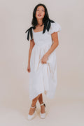 Woman wearing a white dress with black accents against a plain background